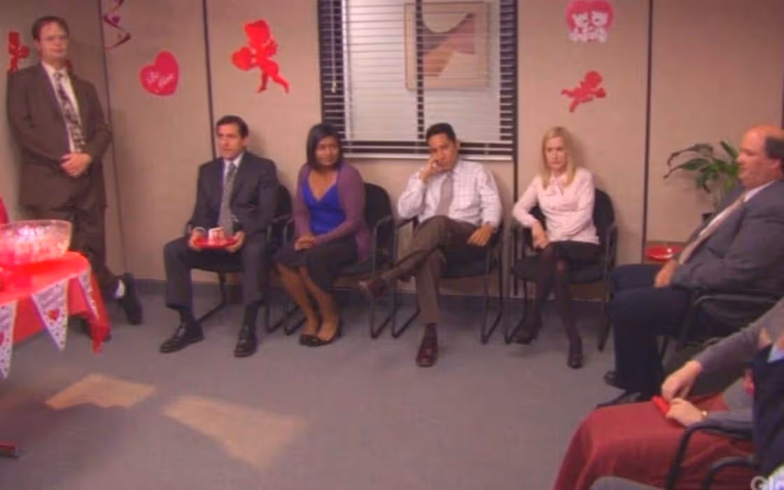 The Office team sitting silently in a meeting room decorated for Valentine's Day, looking bored | Timestripe